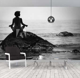 Picture of Young woman sits in a lotus position on a large stone in the sea and meditates her fingers are folded in Prithivi mudra